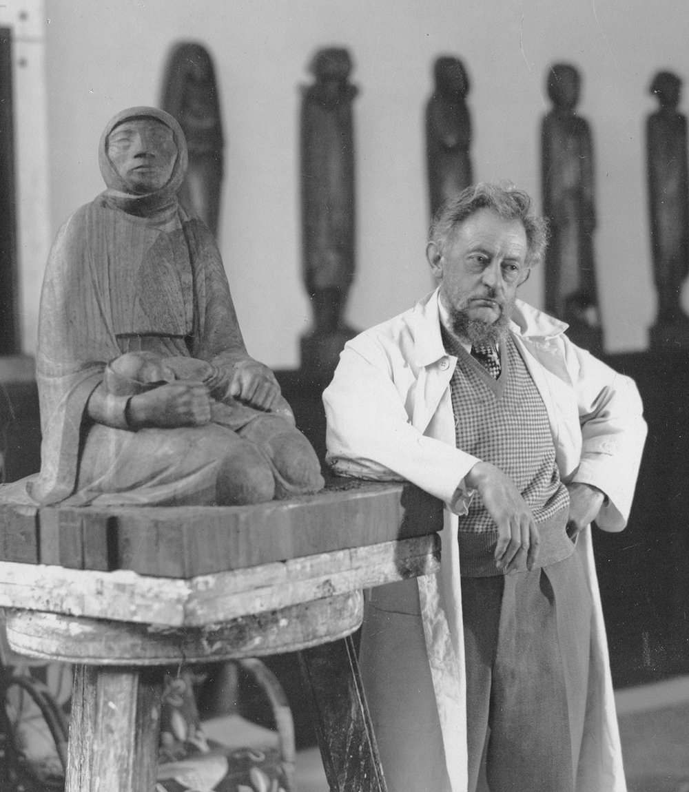 Ernst Barlach in seinem Atelier neben Holzskulptur Mutter und Kind